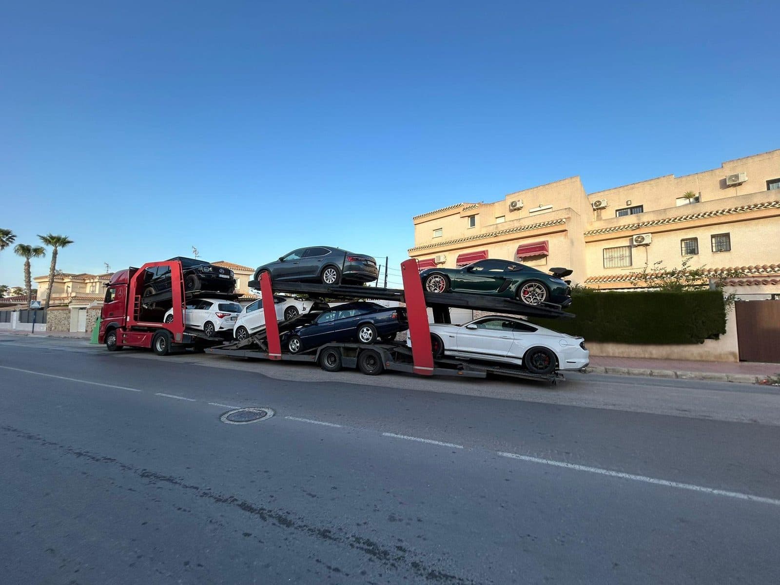 Czerwony autotransporter z samochodami przy palmach na wybrzeżu Hiszpanii